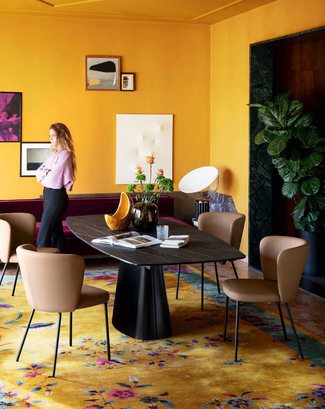 Tavolo Ellisse Connubia sagomato con piano in ceramica noir désir in una sala gialla con tappeto fiorato