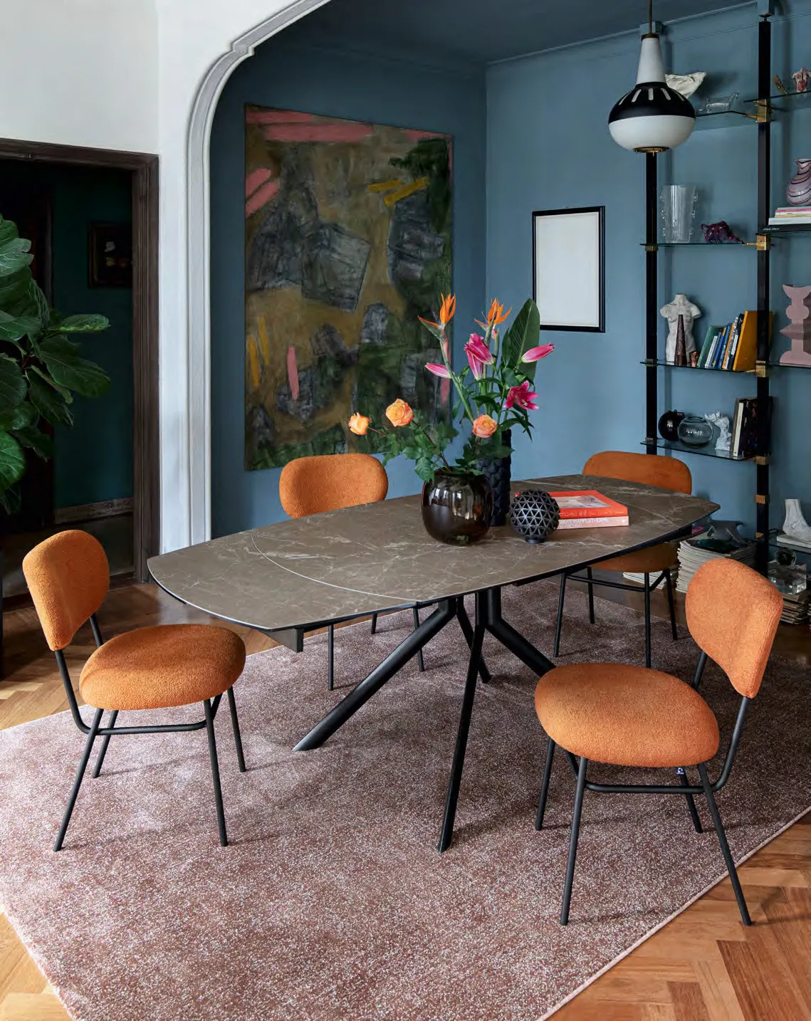 Tavolo Giove Plus Connubia con piano arenaria brown e sedie arancio in una sala con parete blu