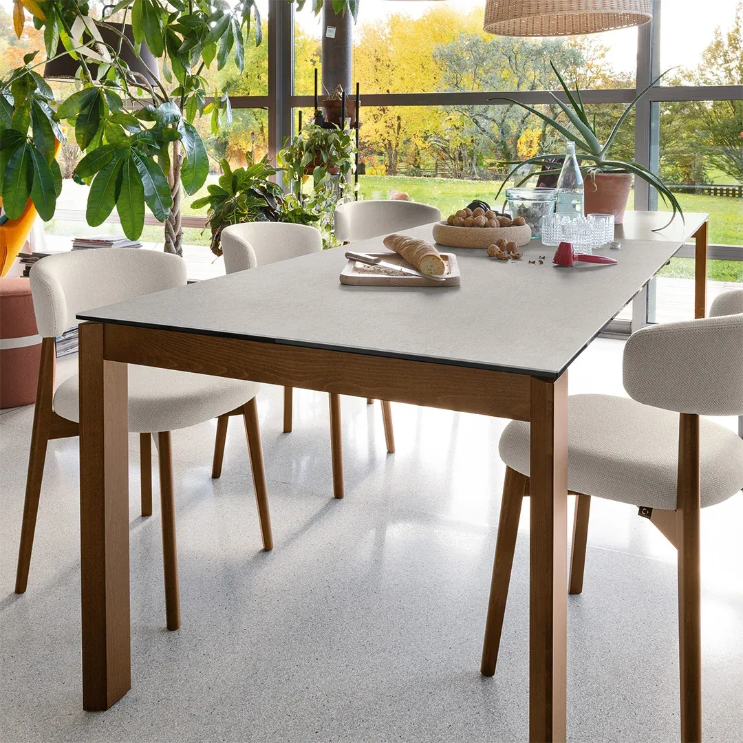 Tavolo Eminence Wood Connubia con gambe color noce e piano chiaro davanti a una vetrata sul giardino
