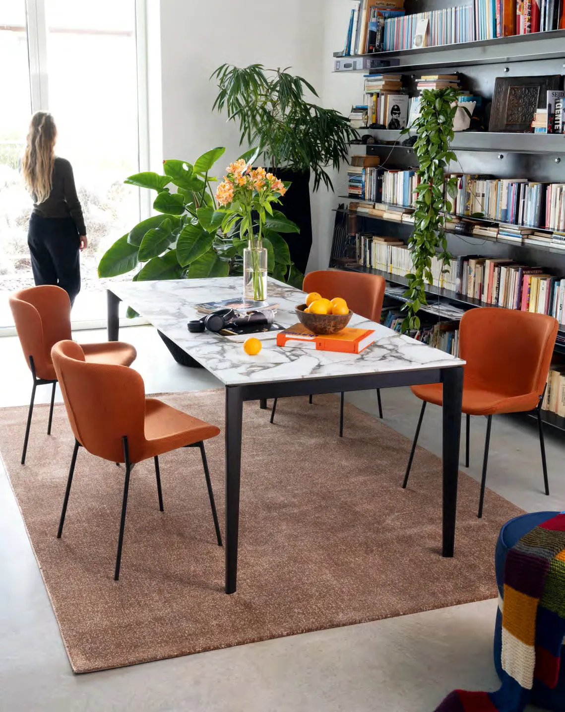 Tavolo Artic Connubia nero con piano in nobilitato arabescato e sedie arancio davanti a una libreria