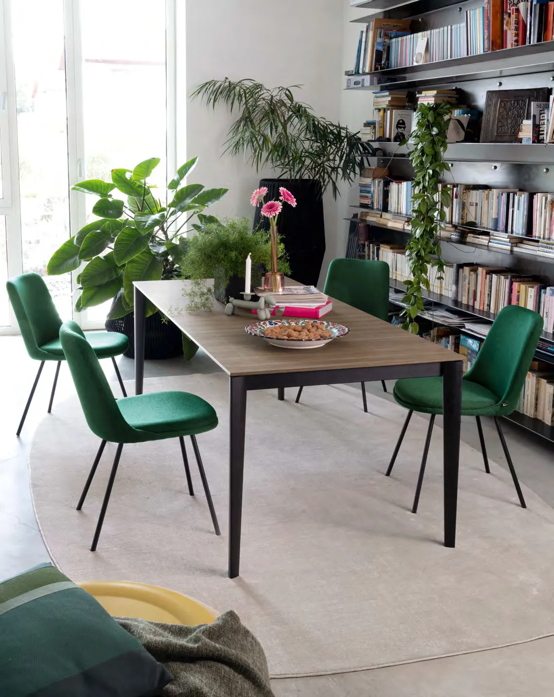 Tavolo Artic Connubia con piano in nobilitato noce e sedie in velluto verde vicino a una libreria