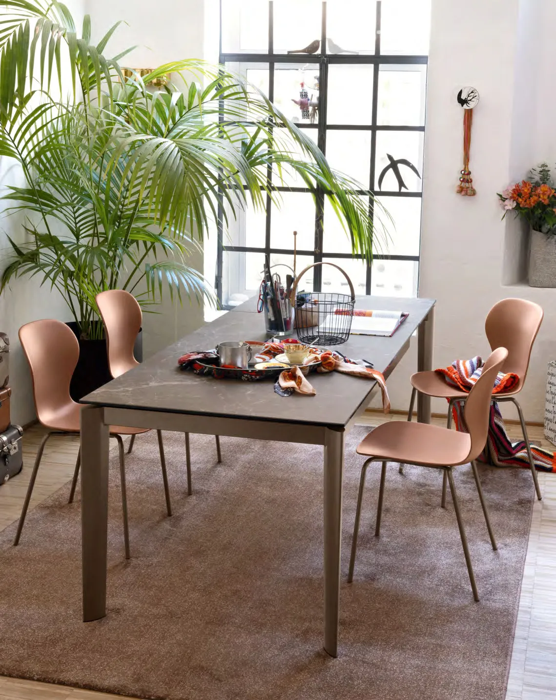 Tavolo Lord Connubia lava con piano arenaria brown e sedie Ops terracotta davanti a una vetrata