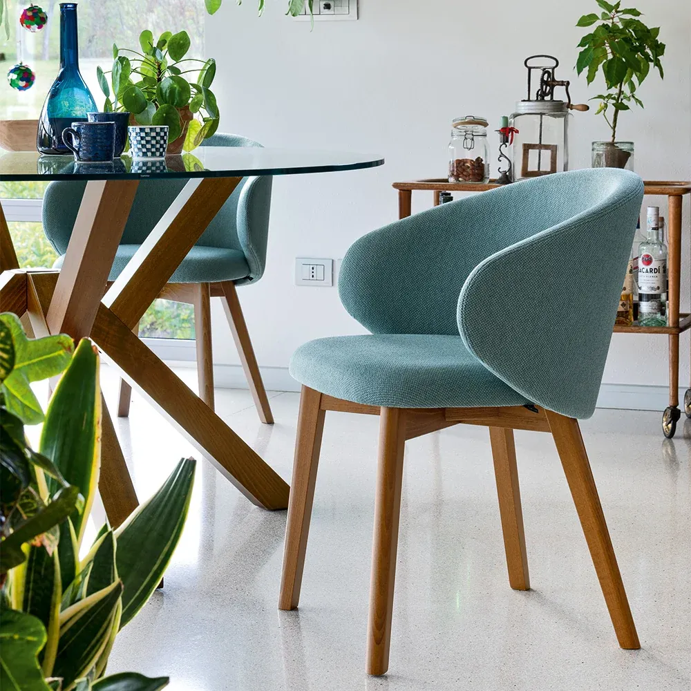 Tavolo Mikado Connubia tondo in vetro con base in legno e poltroncina azzurra in una cucina