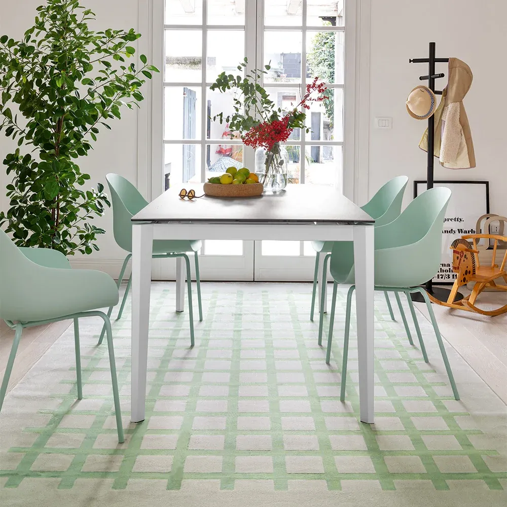 Tavolo Pentagon Fast Connubia bianco con sedie verde menta su un tappeto a quadri davanti a una portafinestra