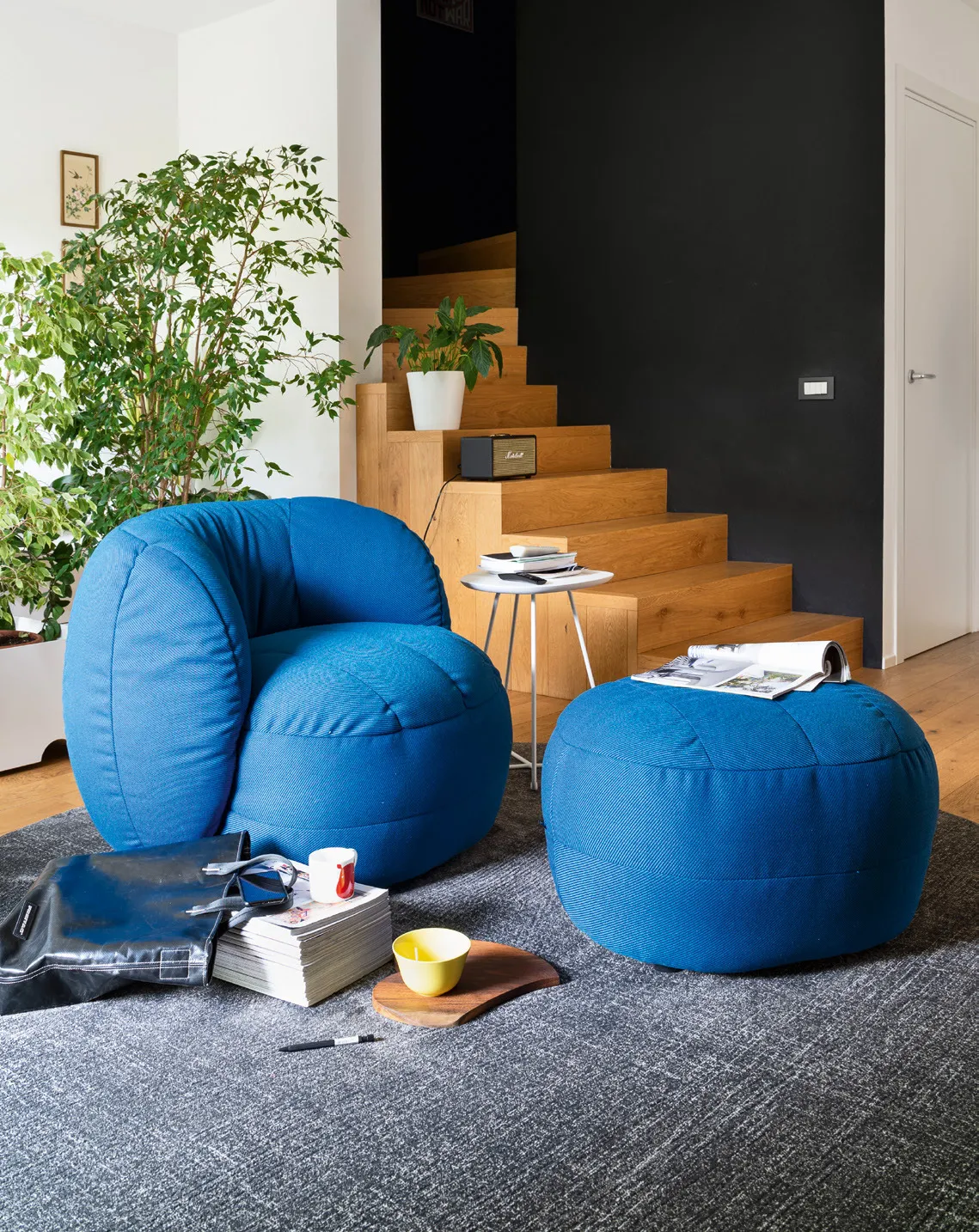 Poltrona Reef Connubia in tessuto Oceanic blu con pouf coordinato su un tappeto grigio, scala in legno
