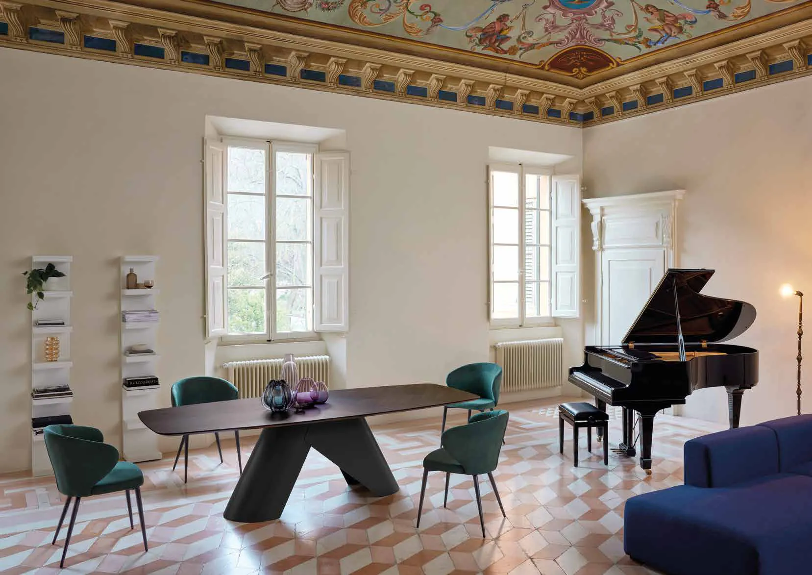 Tavolo Orion Friulsedie con piano in rovere a spina e poltroncine verdi in un salone con pianoforte