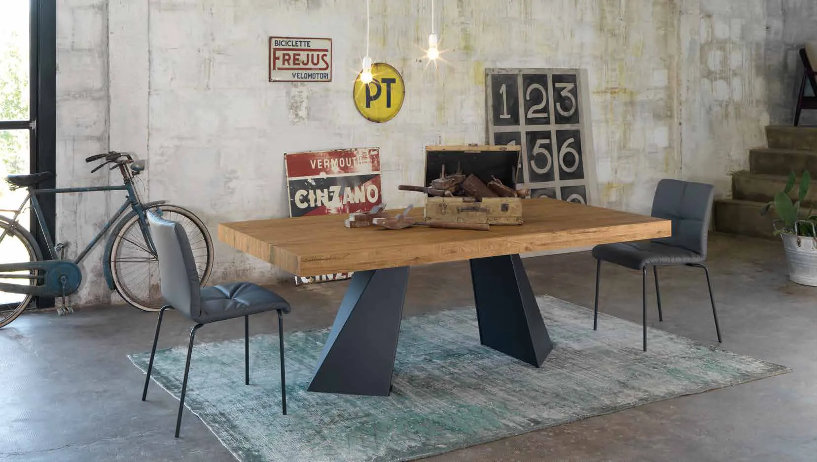 Tavolo Portland Friulsedie Syncro antracite con piano effetto rovere davanti a un muro in pietra
