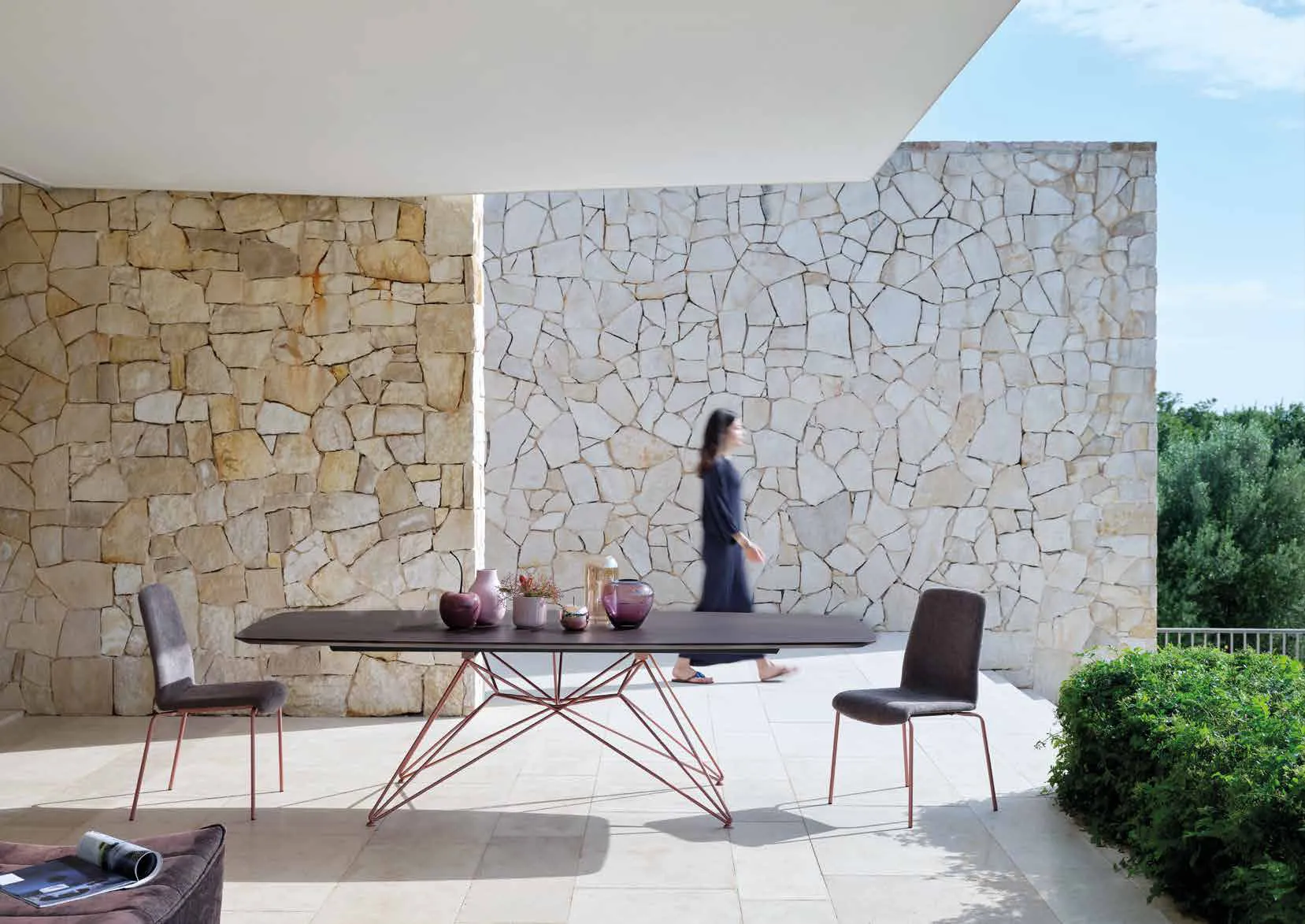 Tavolo Atlante Friulsedie con base in filo oro rosa sotto una pergola davanti a un muro in pietra