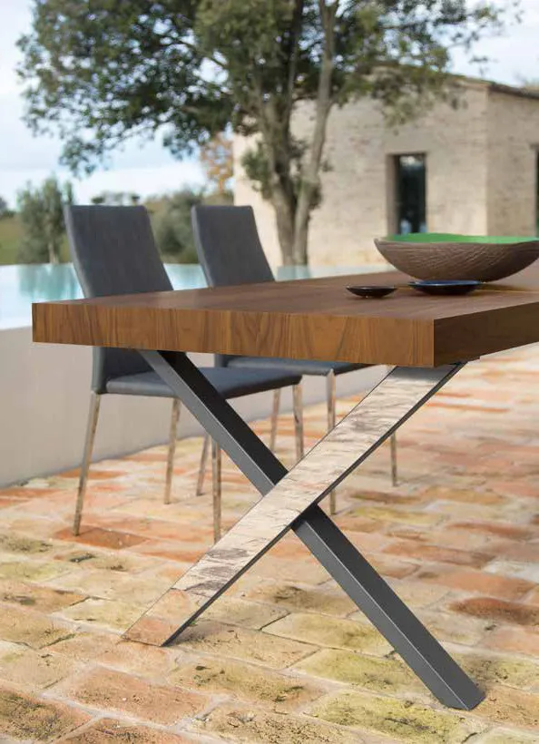 Gambe incrociate con carter inox lucido del tavolo Memphis Friulsedie, piano in noce