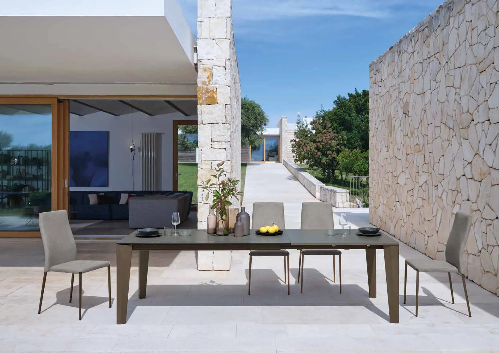 Tavolo superallungabile Spencer Friulsedie in ottone con piano Keramic su una terrazza in pietra