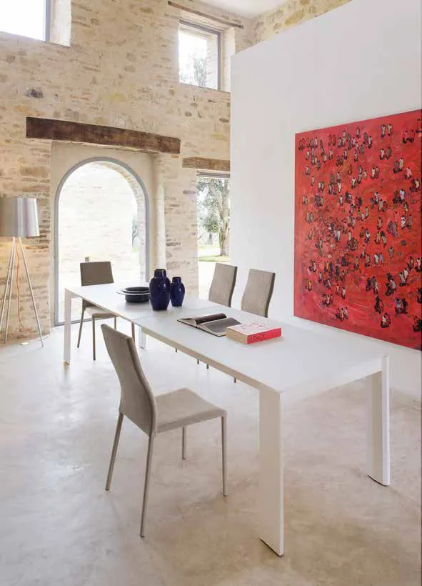 Tavolo Madison Friulsedie laccato bianco con piano in vetro extrabianco in una sala con muro in pietra