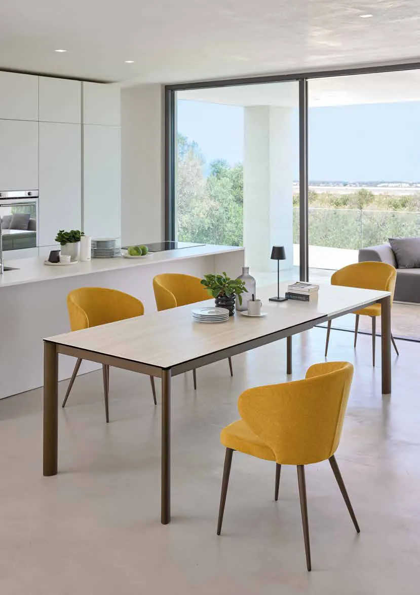 Tavolo Matisse Friulsedie in ottone con piano Keramic Travertino bianco e poltroncine gialle in cucina