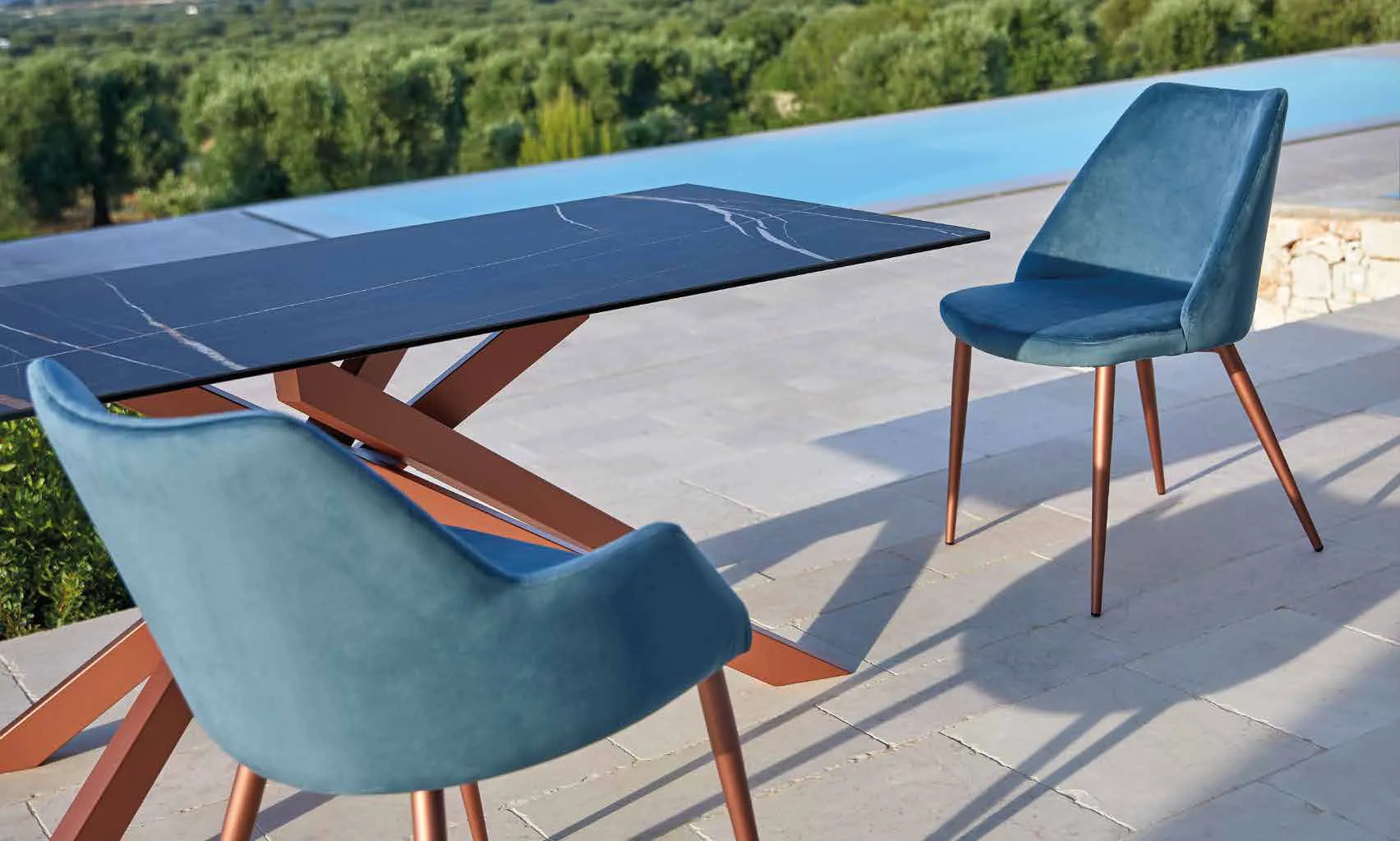 Poltroncina Janis e sedia Gea Friulsedie in velluto blu attorno a un tavolo su una terrazza