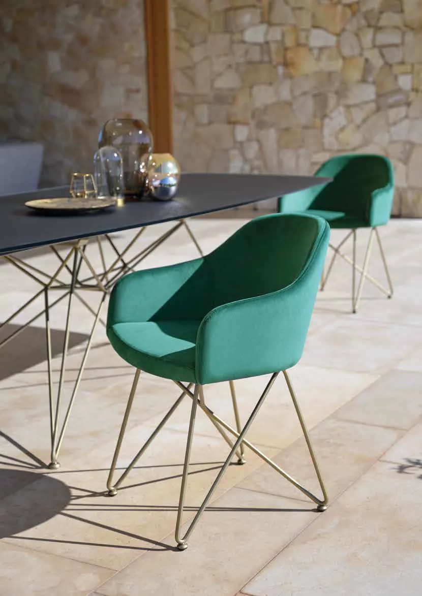 Poltroncina Demetra Friulsedie in velluto verde con base in tondino oro antico accanto al tavolo