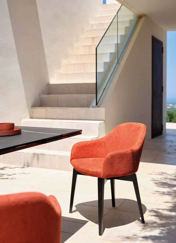 Poltroncina Demetra Friulsedie in tessuto terracotta con gambe in frassino nero vicino a una scala