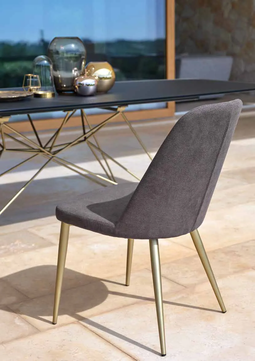 Sedia Noah Friulsedie in tessuto grigio con gambe oro antico accanto al tavolo Atlante
