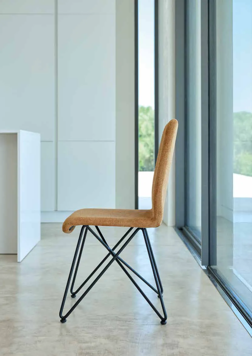 Sedia Mia Friulsedie in tessuto caramel con base in tondino nero vicino a una vetrata