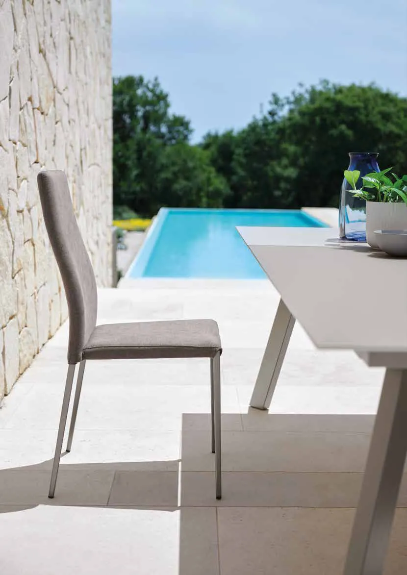 Sedia Tracy Friulsedie in tessuto taupe con gambe titanio accanto a un tavolo vicino alla piscina