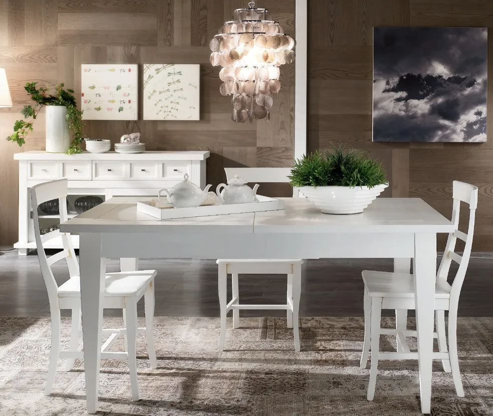 Tavolo allungabile Maison Imba laccato bianco con sedie bianche sotto un lampadario
