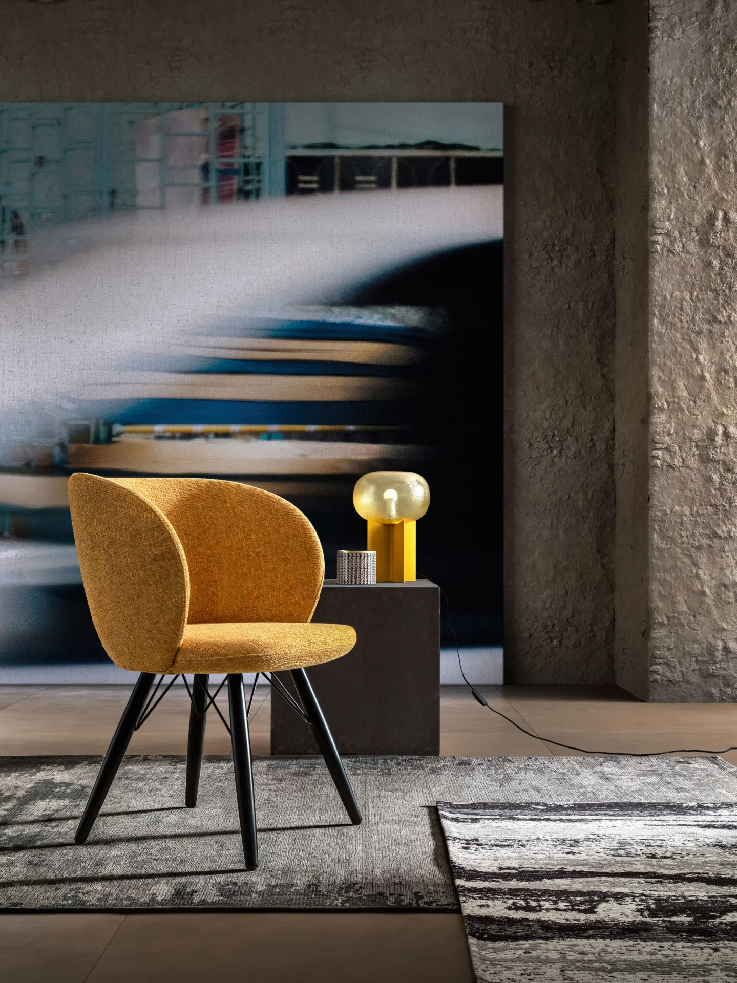 Poltroncina Agave Samoa in tessuto giallo senape su gambe nere, accanto a una lampada da tavolo