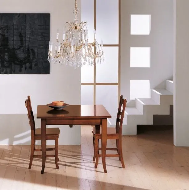 Tavolo quadrato Trend Style Imba in noce con due sedie sotto un lampadario di cristallo