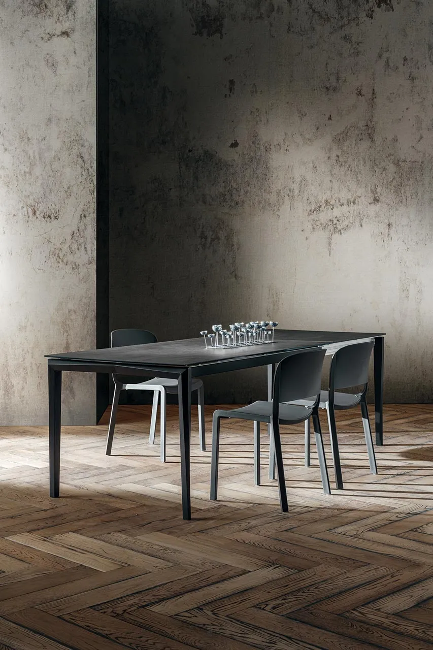 Tavolo Bill La Primavera nero con sedie grigie su parquet a spina