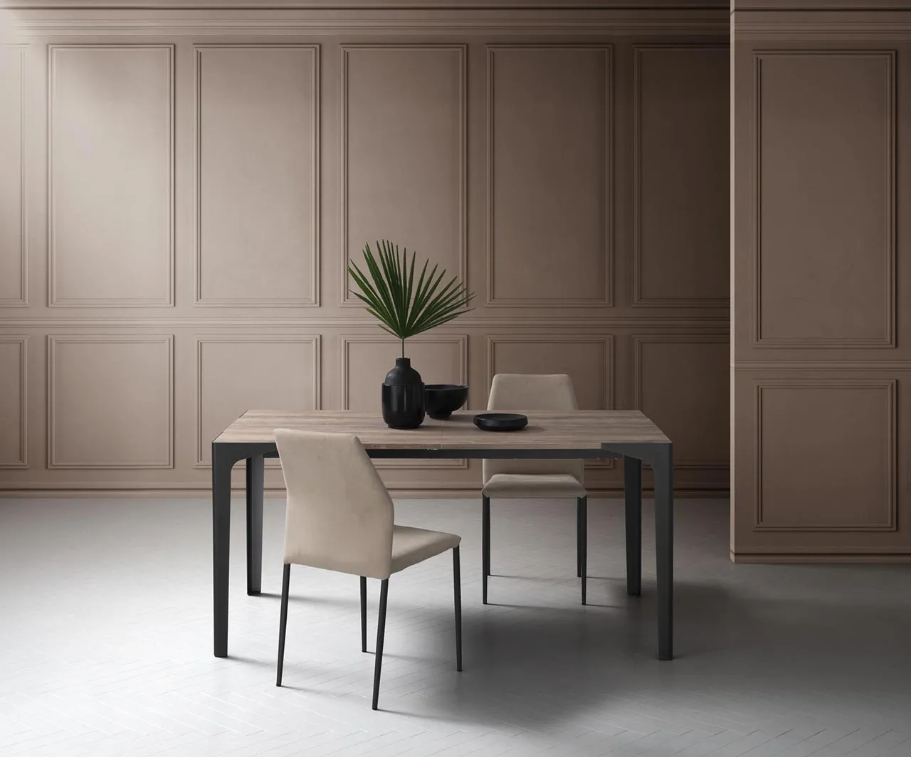 Tavolo Ettore La Primavera chiuso con due sedie beige e boiserie sullo sfondo