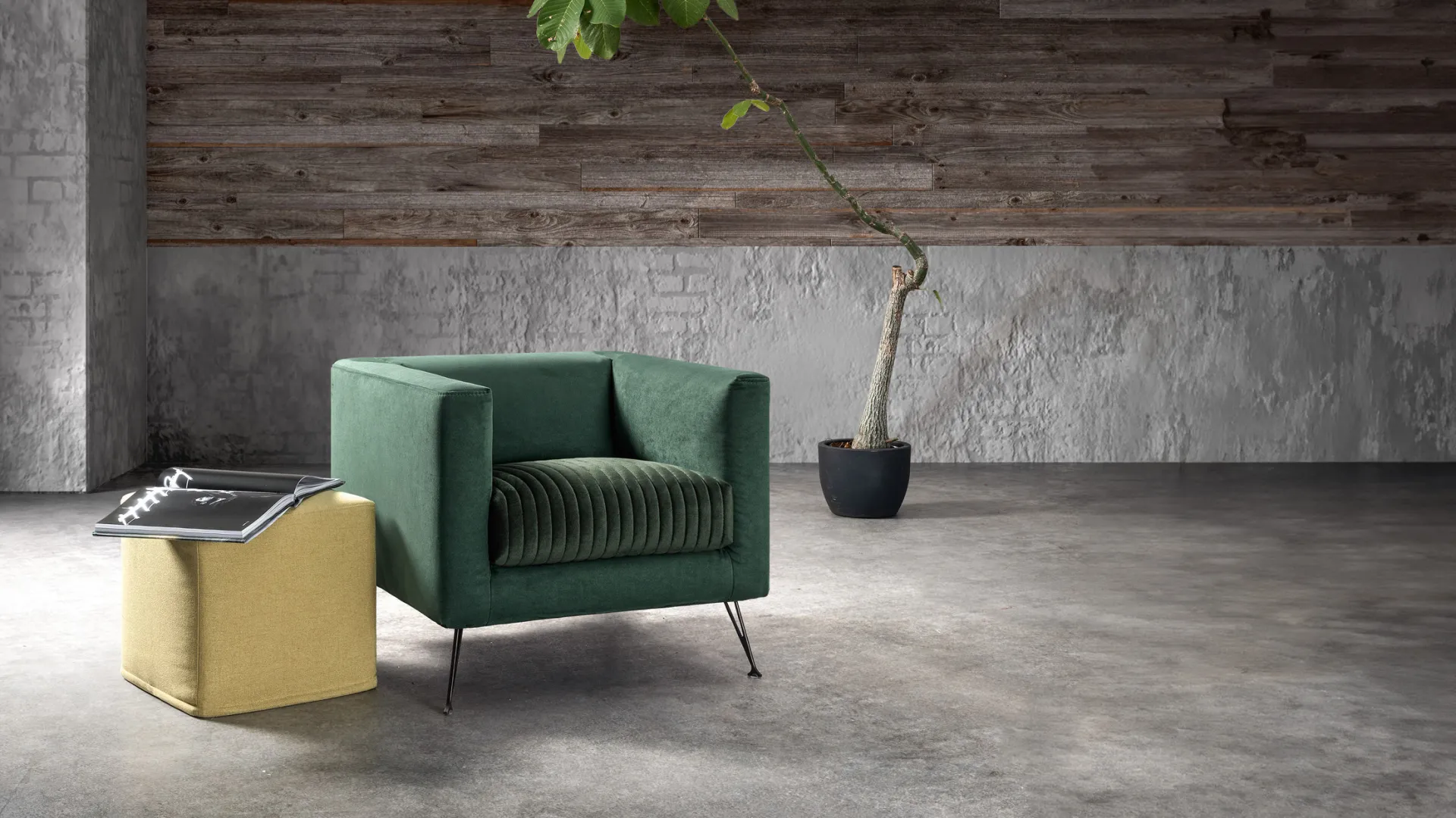 Poltrona Synthesis Samoa in velluto verde con seduta a cannette, accanto a un pouf giallo