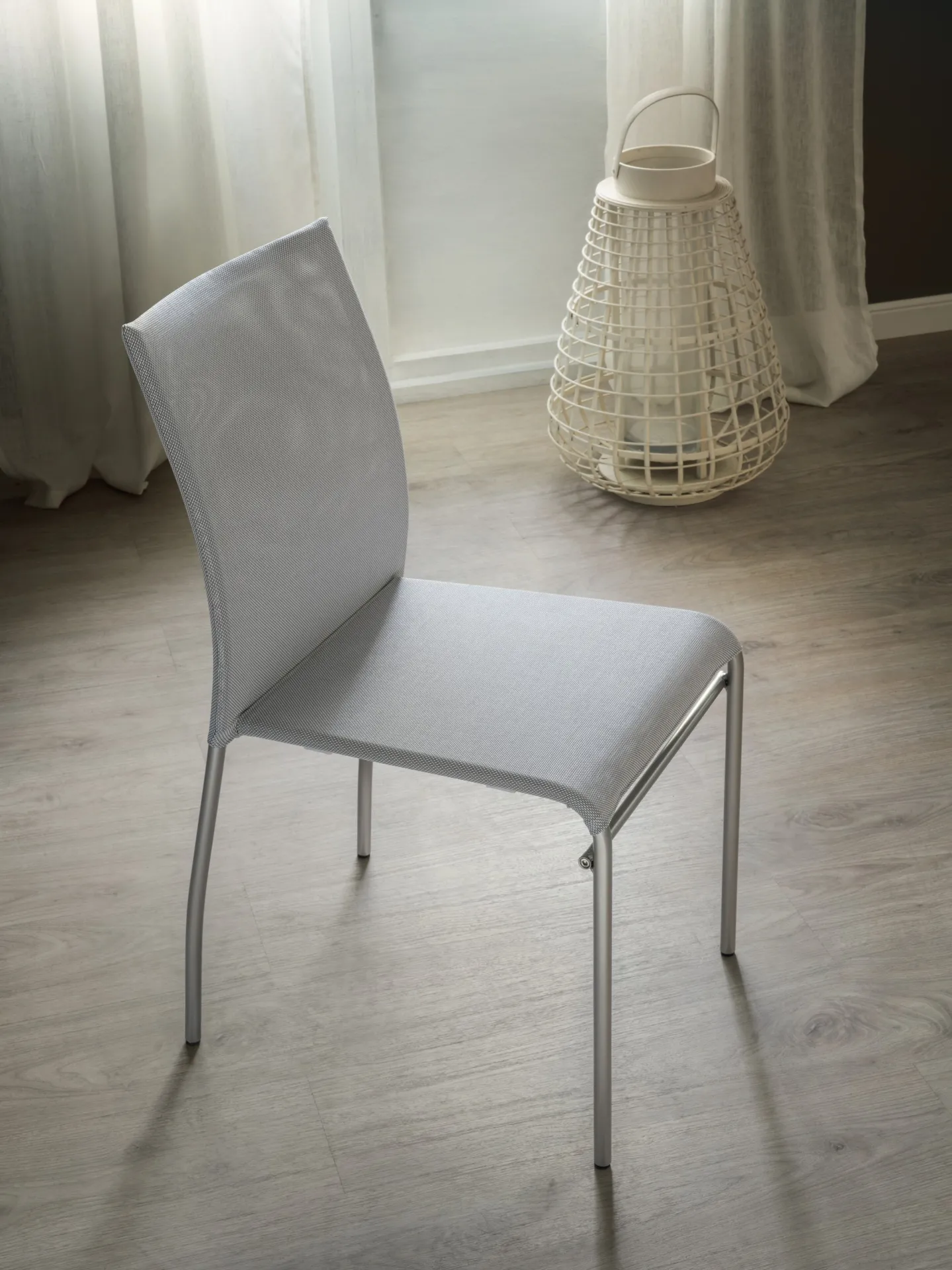 Sedia Avenue Scavolini grigio chiaro su pavimento in legno accanto a una lanterna