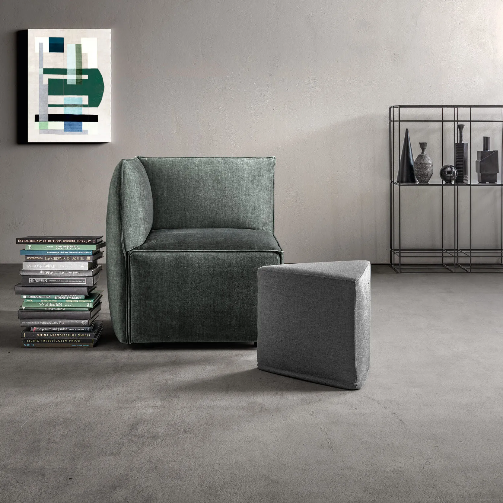 Poltrona Craft Samoa verde salvia con pouf triangolare grigio, accanto a una pila di libri