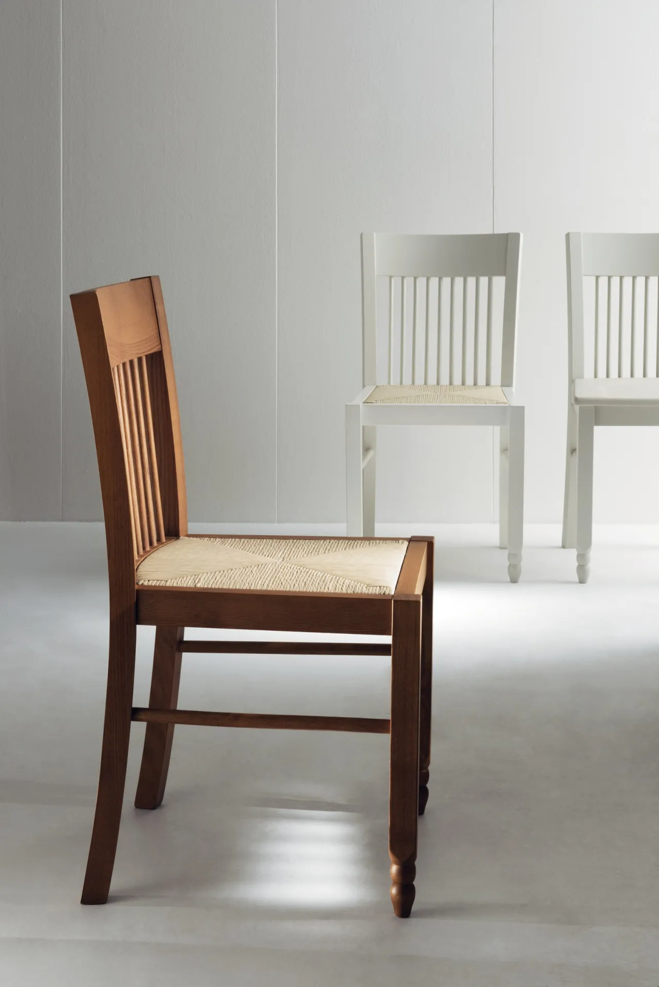 Sedia Gea Scavolini color noce con fondino in paglia, con sedie bianche sullo sfondo