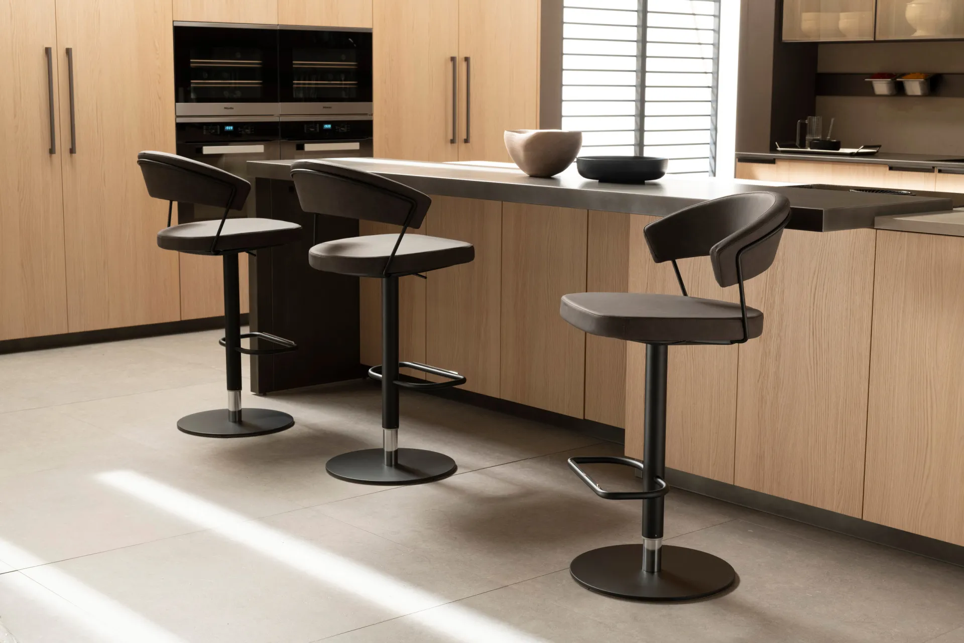 Sgabelli Great con piedistallo Scavolini scuri lungo una penisola in legno chiaro