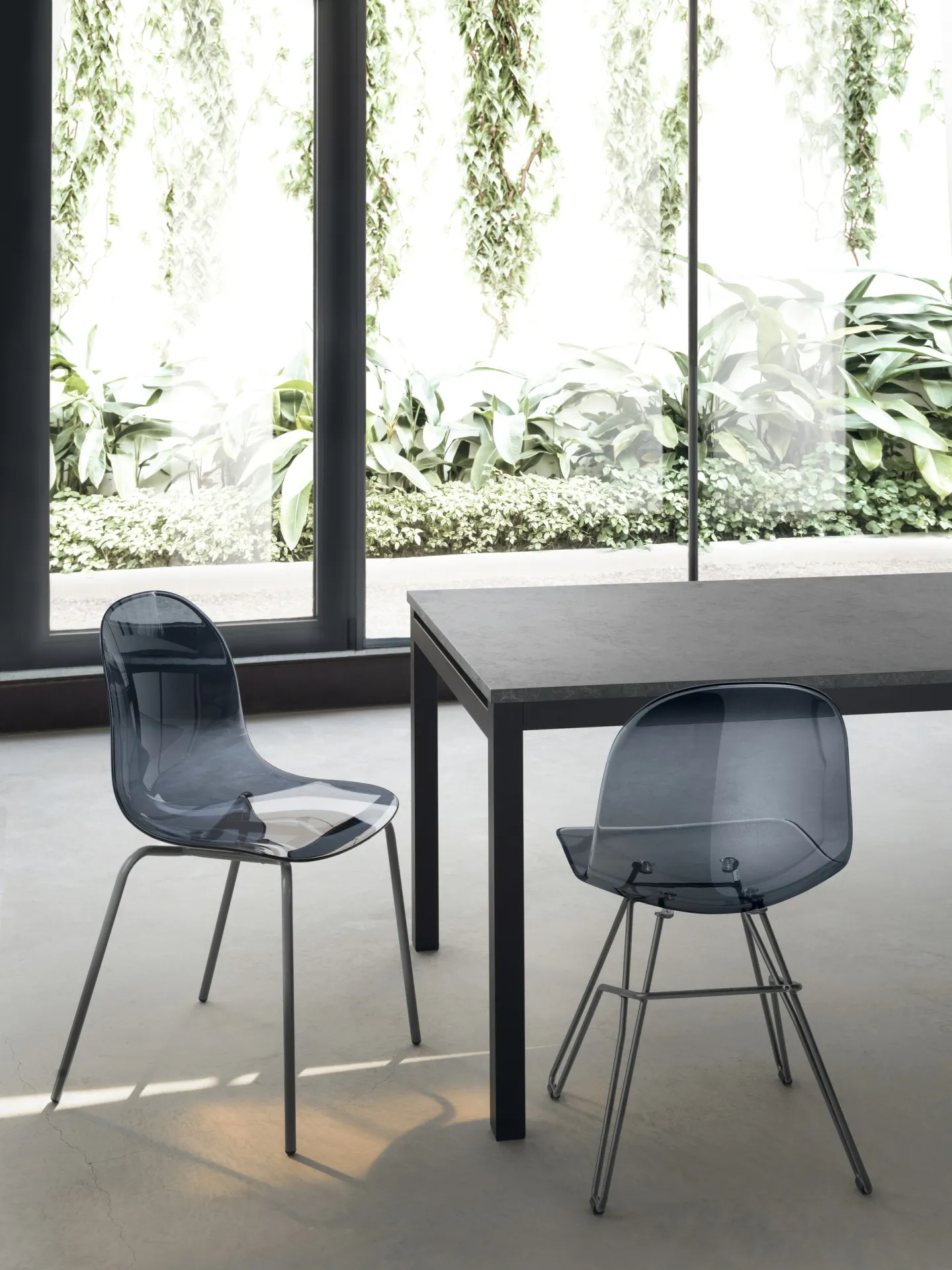Sedie Hero Pop Scavolini fumé trasparenti accanto a un tavolo vicino a una vetrata