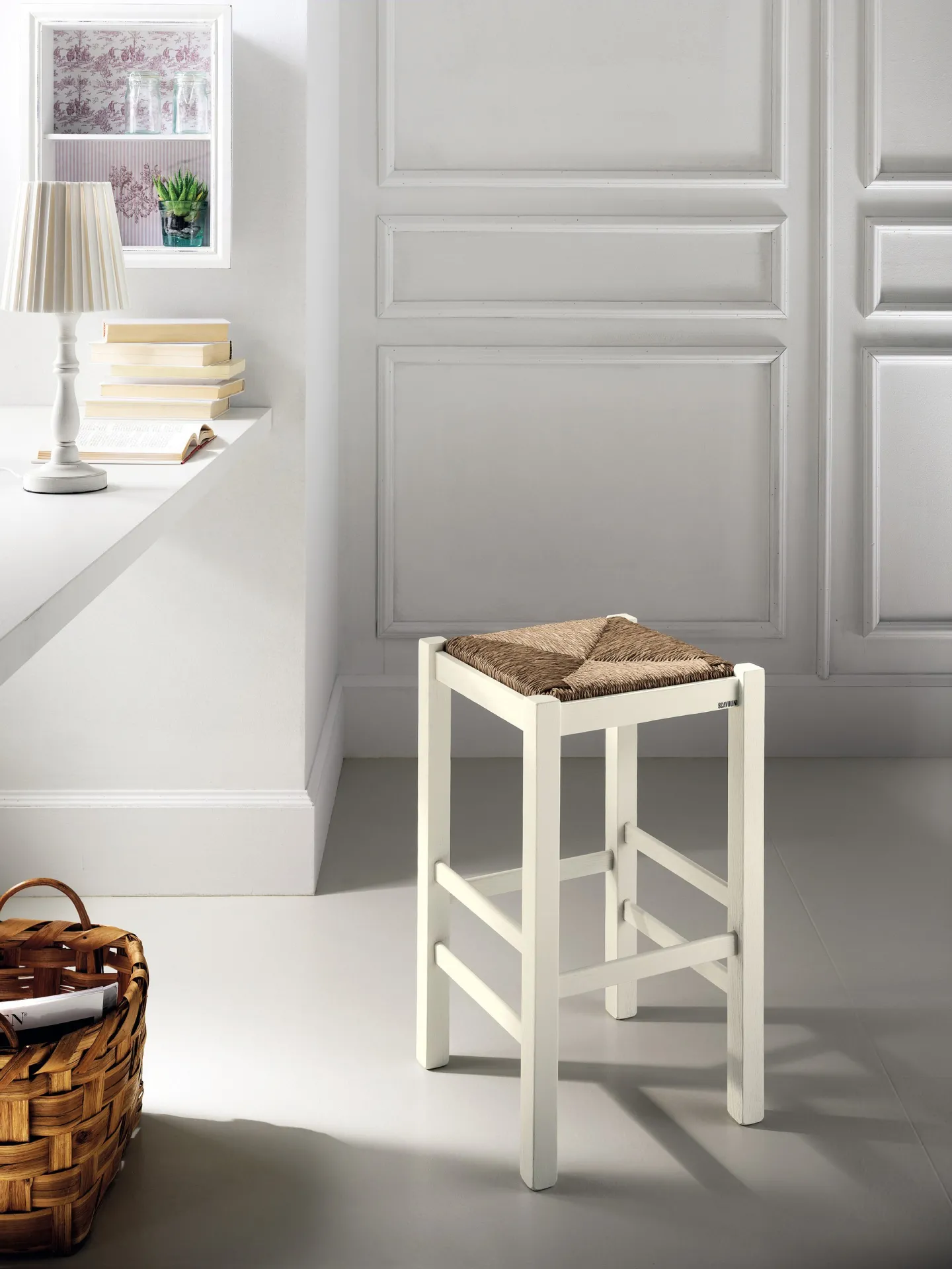 Sgabello Margot Scavolini laccato bianco con seduta in paglia vicino a un cesto in vimini