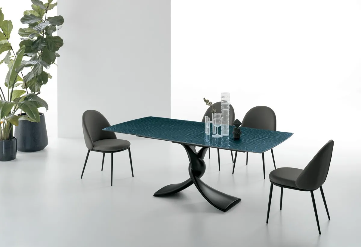 Tavolo Twist Target Point con base intrecciata nera e piano blu, sedie scure fra le piante