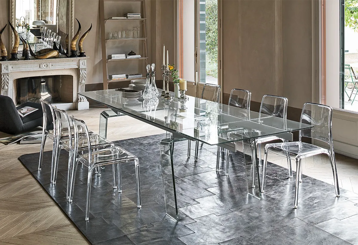 Tavolo Crystal Plus Target Point in vetro trasparente con sedie trasparenti davanti a un camino