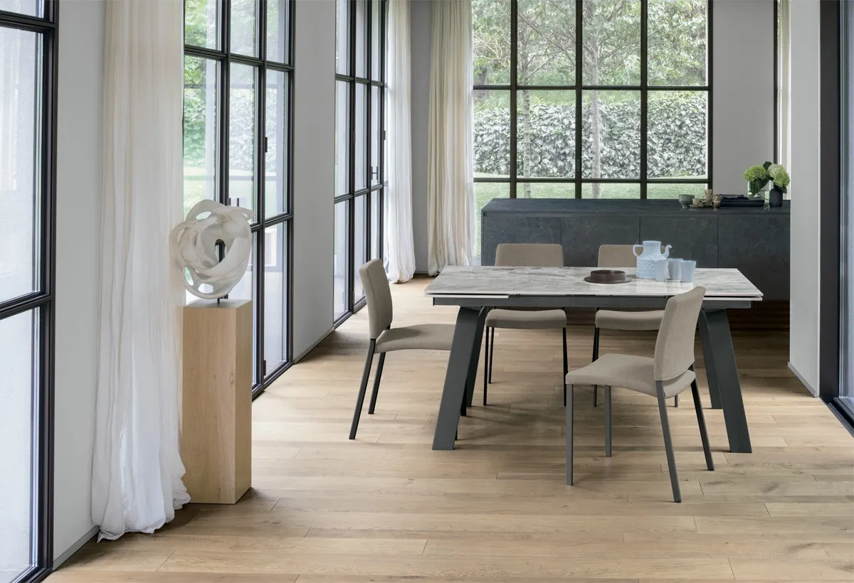 Tavolo Marte Target Point con piano effetto marmo e gambe scure, sedie beige davanti alle vetrate