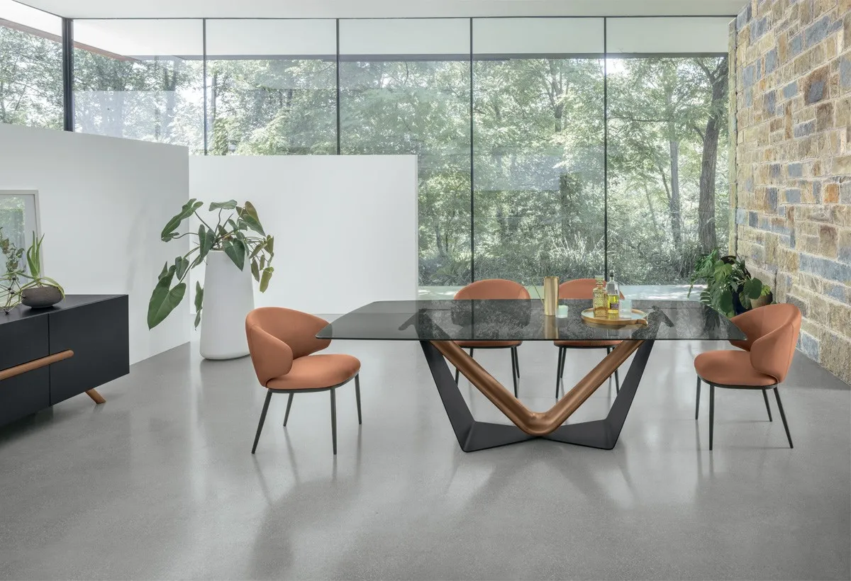 Tavolo Velar Target Point con base a V color rame e piano in vetro scuro, sedie arancio