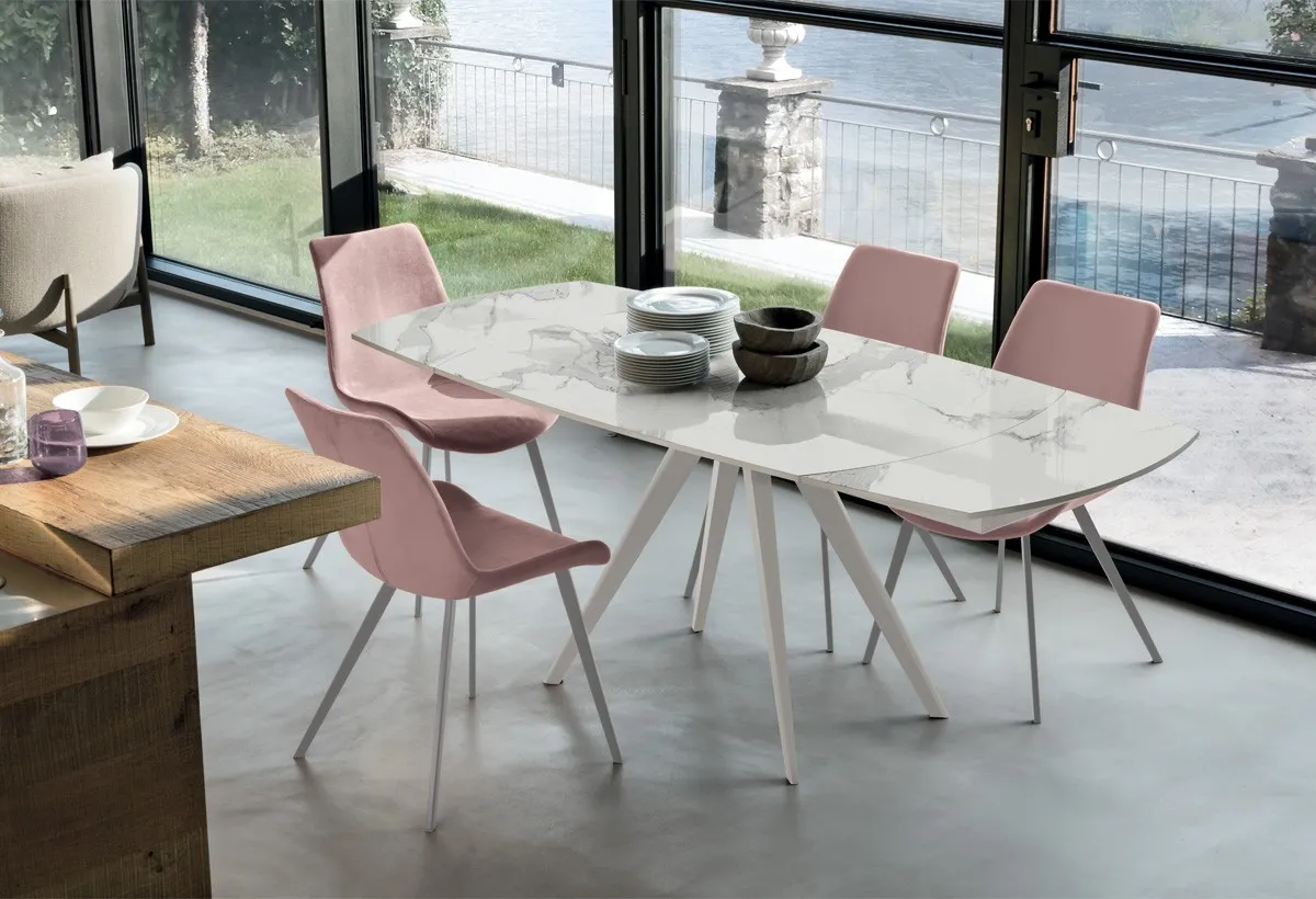 Tavolo Vortice Target Point bianco con piano effetto marmo e sedie rosa davanti al lago