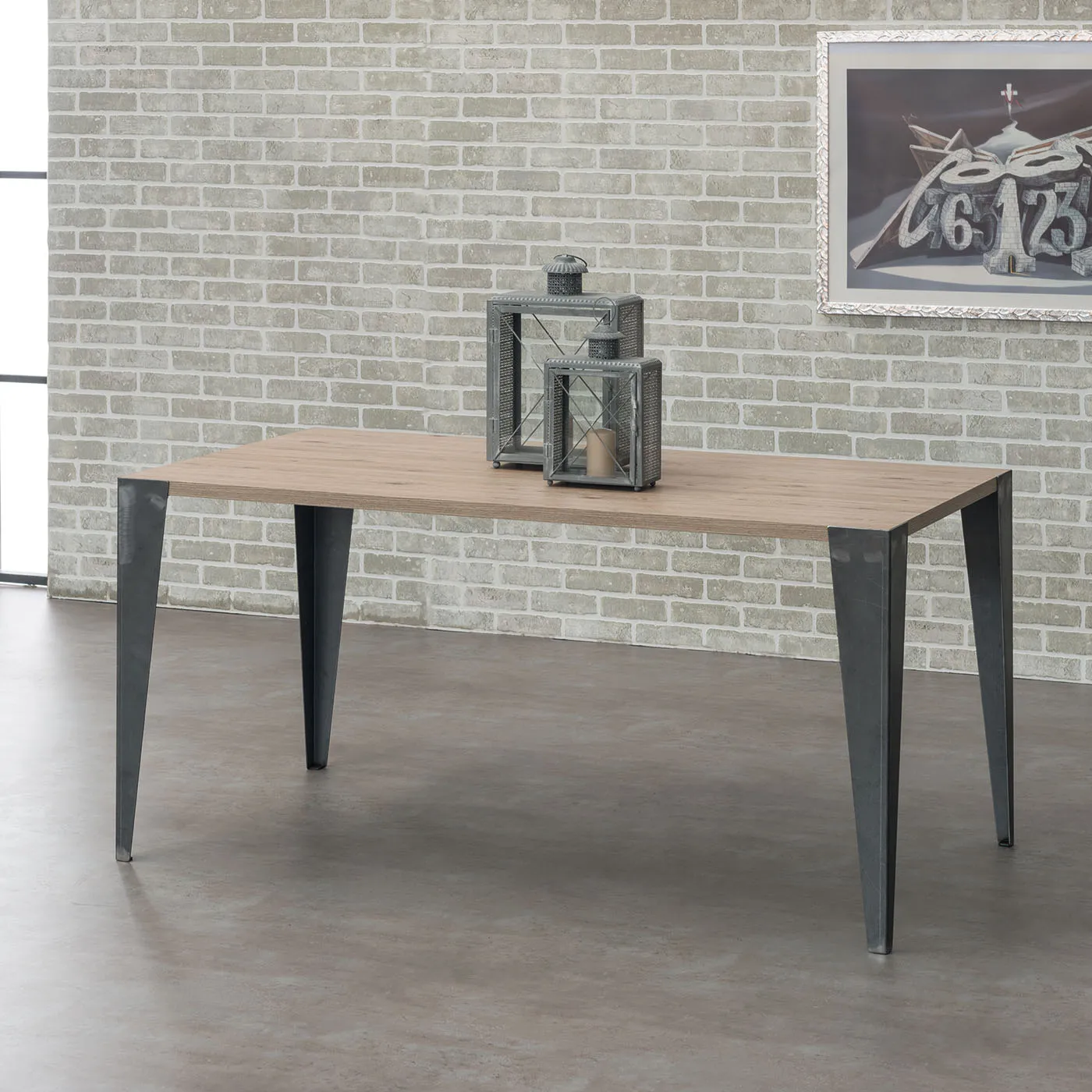 Tavolo Genio Tecnolegno con piano effetto legno chiaro e gambe nere davanti a un muro in mattoni