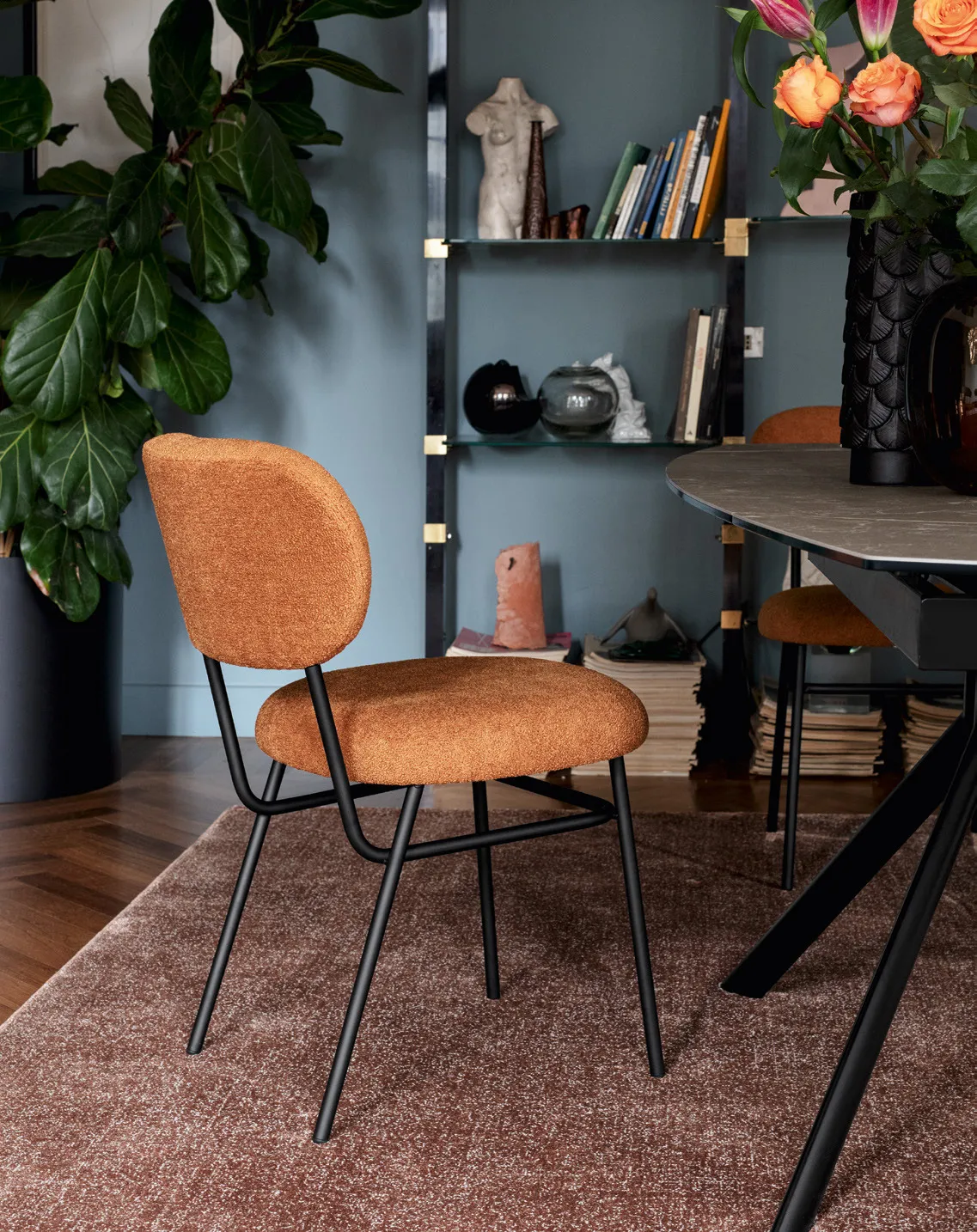 Sedia Pad Connubia in tessuto ruggine con telaio nero accanto a un tavolo con piano in ceramica scura
