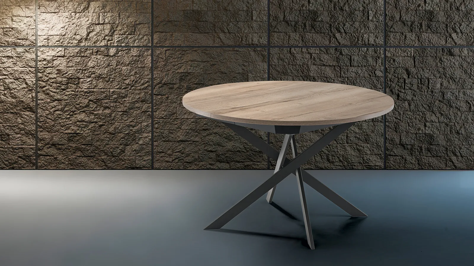 Tavolo San Diego Tecnolegno rotondo effetto legno davanti a una parete in pietra