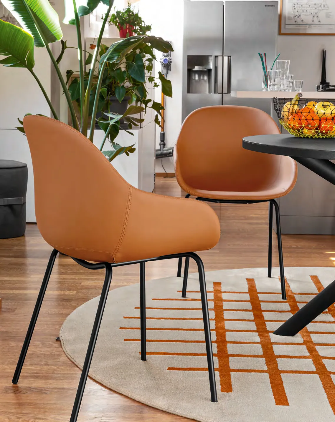 Poltroncine Academy AC Connubia in similpelle cognac con gambe nere su un tappeto a righe arancio