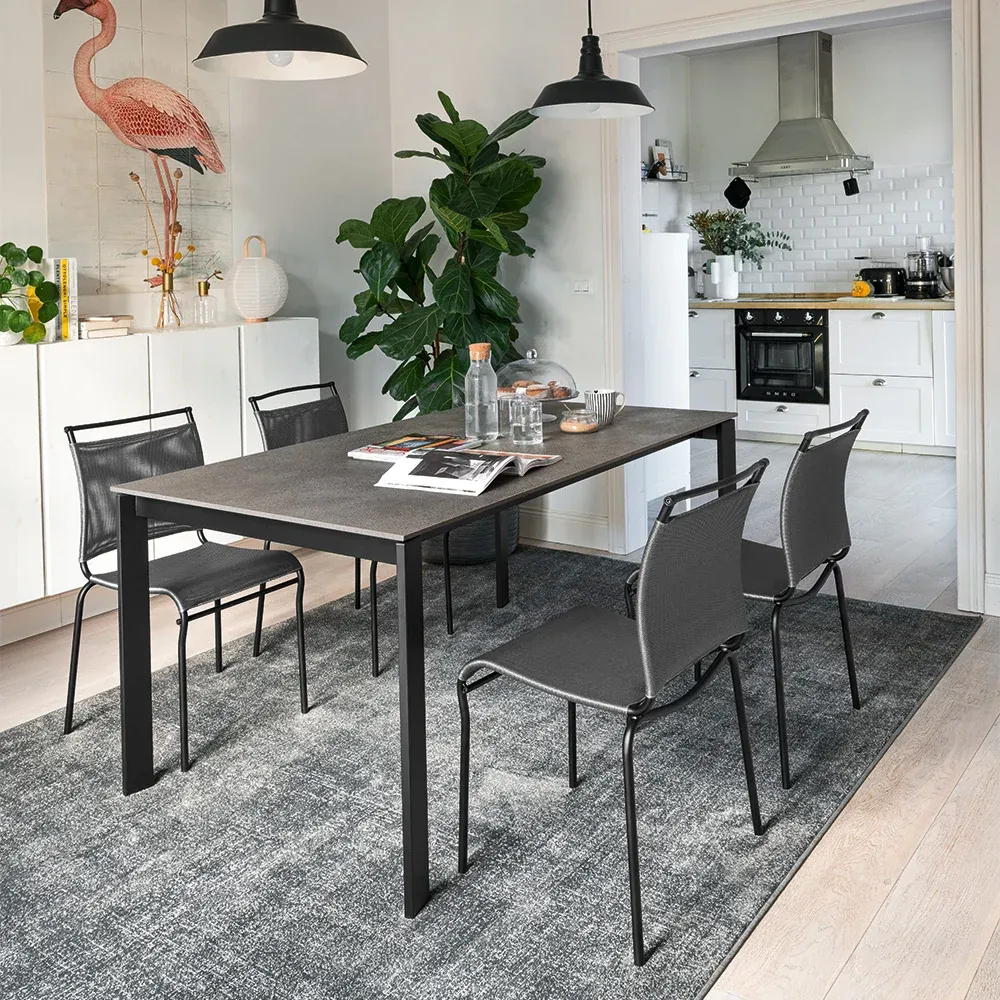 Tavolo da pranzo scuro con sedie Air Connubia nere su un tappeto grigio, cucina sullo sfondo