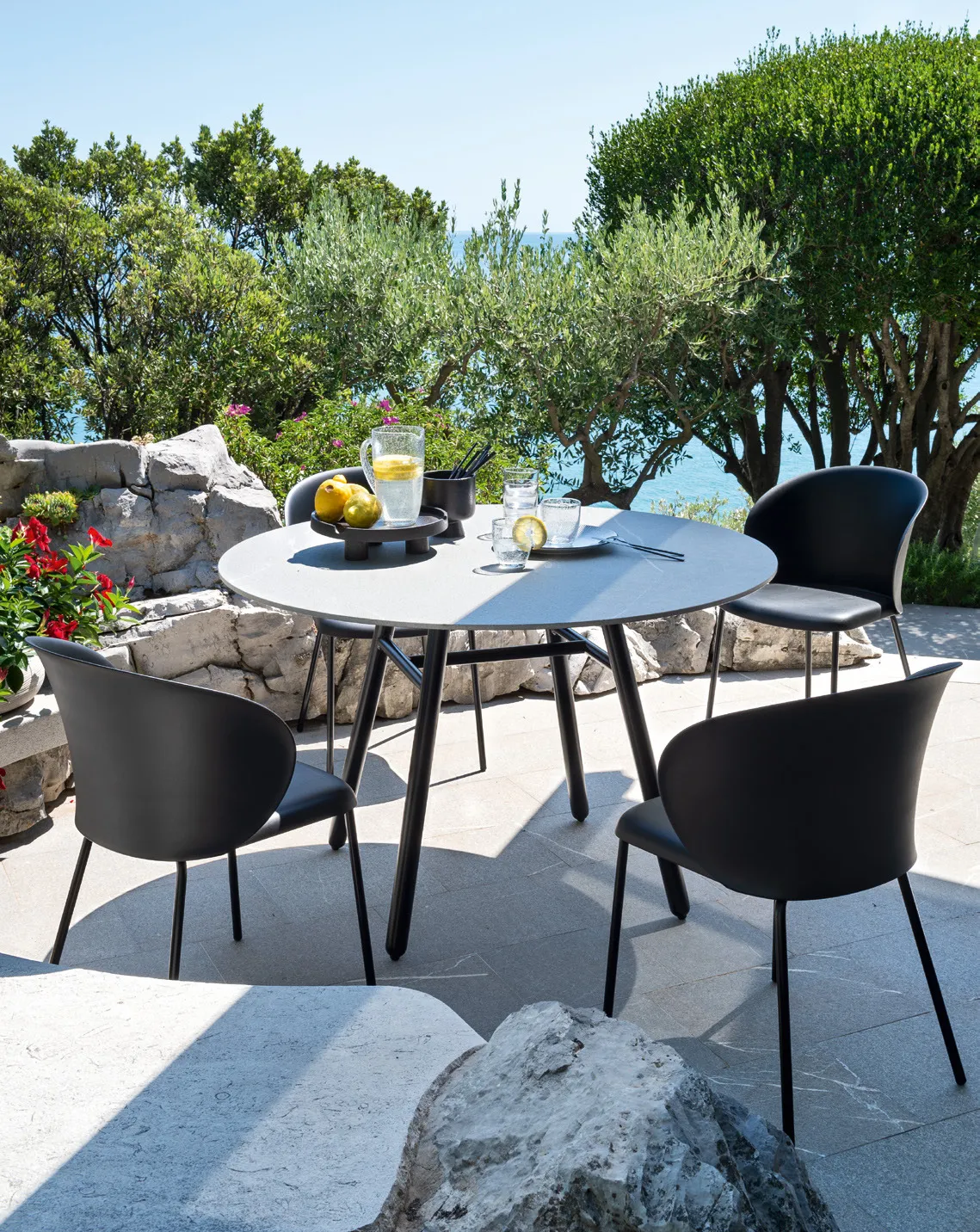 Sedie Tuka outdoor Connubia nere attorno a un tavolo rotondo su una terrazza con vista sul mare