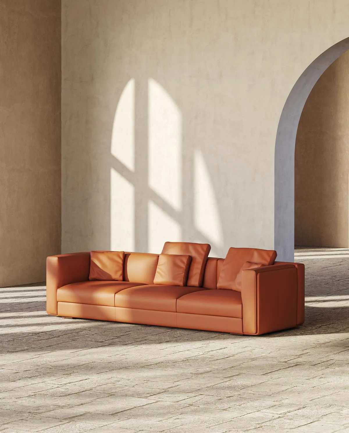 Divano Russell Frezza in pelle cognac con cuscini davanti a un arco