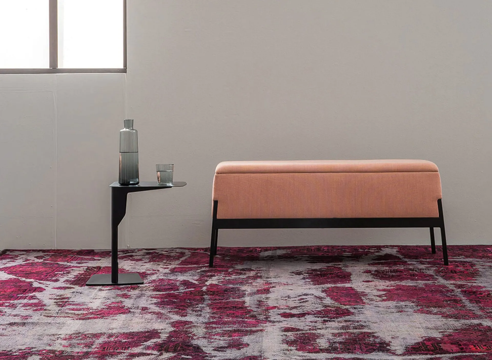 Tavolino Metal Table Frezza nero accanto a una panca imbottita rosa su tappeto