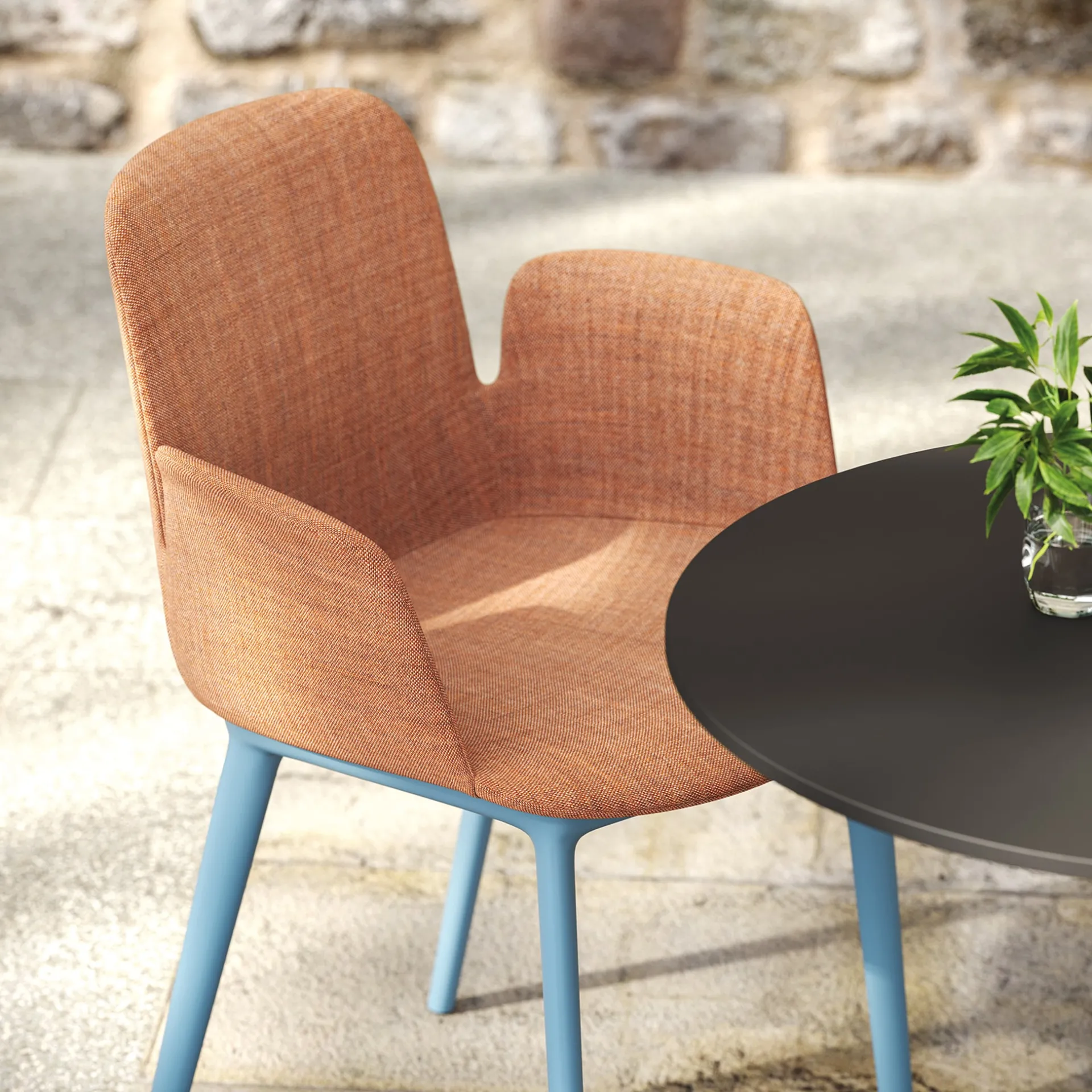 Poltroncina Fior di Loto Upholstered Frezza arancio su gambe azzurre accanto a un tavolino