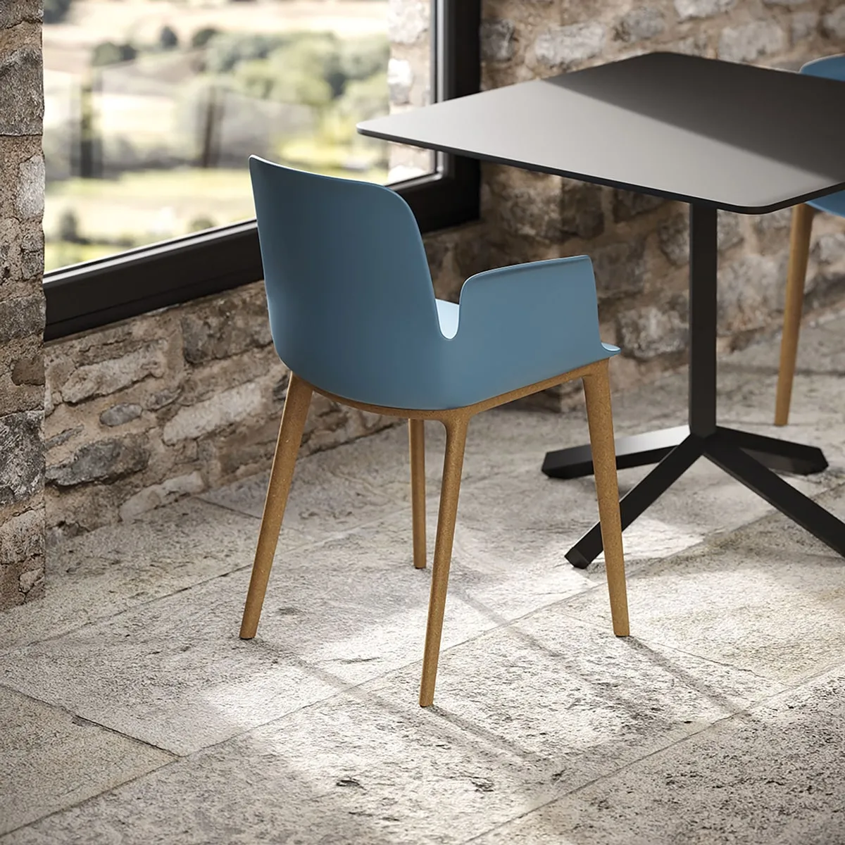 Poltroncina Fior di Loto Plastic Frezza azzurra su gambe in legno accanto a un tavolo