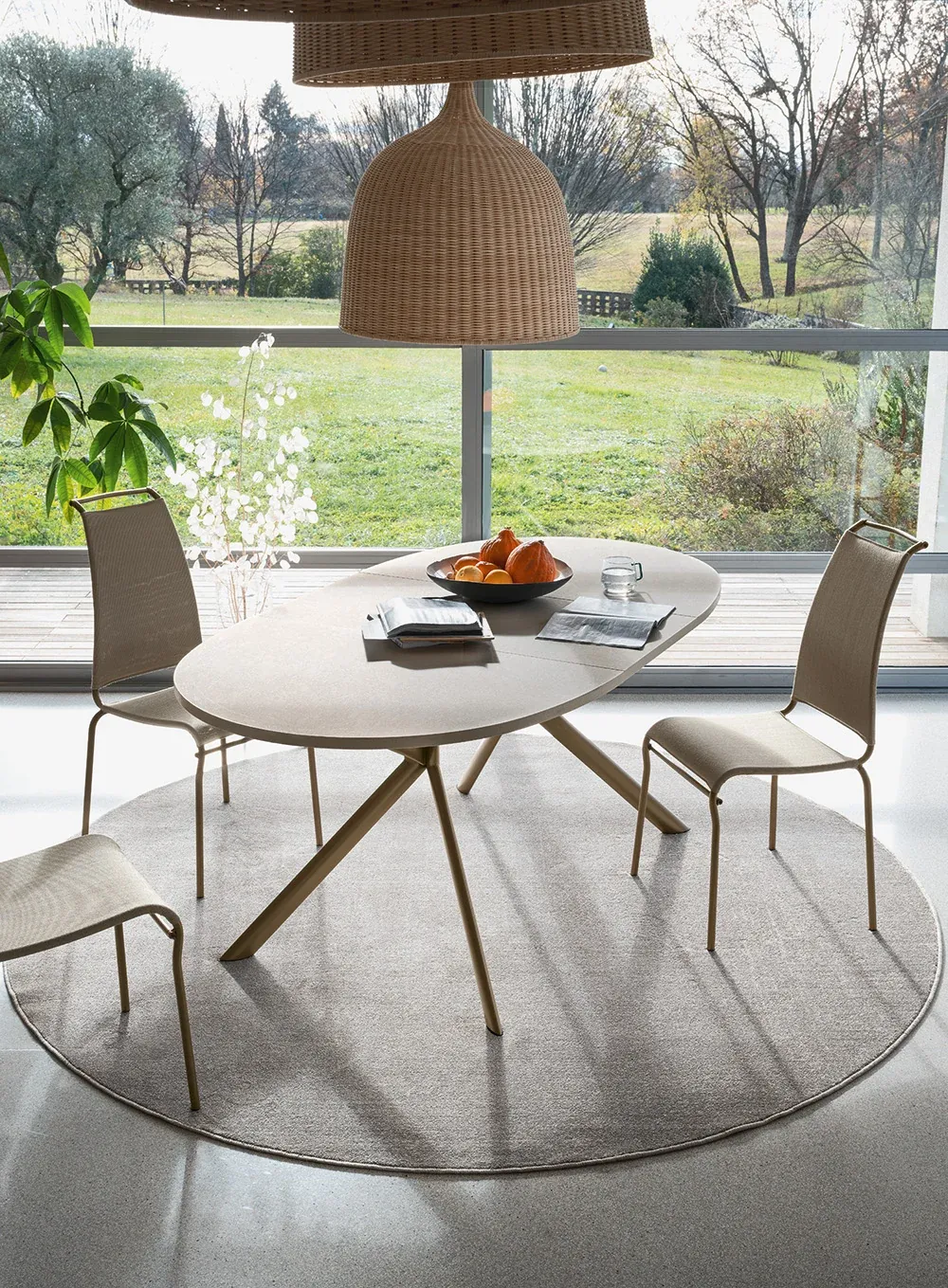 Tavolo rotondo con sedie Air High Connubia sotto una lampada in vimini, con vista sul giardino